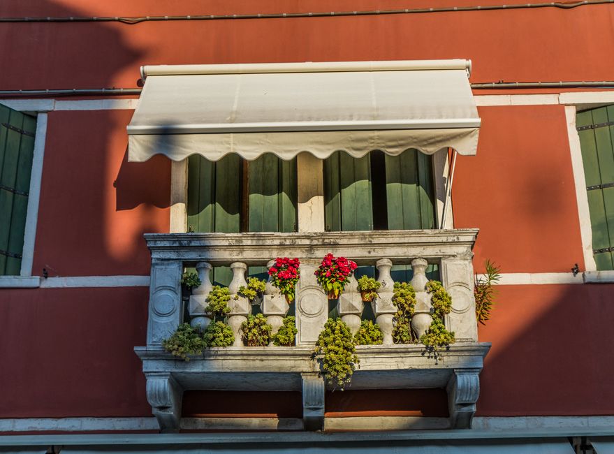 A picturesque stone balcony with vibrant flowers in Chioggia, Italy.